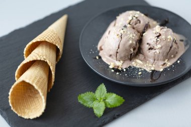 Çikolatalı dondurma ve waffle ahşap bir masa üzerinde siyah bir plaka üzerinde boynuz
