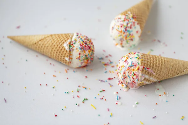 Waffle cone with white ice cream and sweet sprinkles on a light background