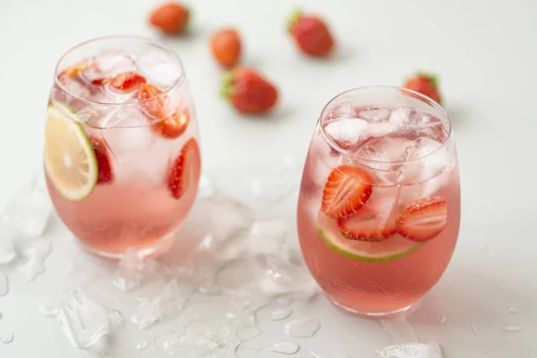 Glass of strawberry lemonade with pieces of strawberry, lime and fresh mint. Fresh summer bright cocktail.