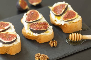 Ricotta sandviç, taze incir, ceviz ve siyah bir zemin üzerine kayrak bir tabakta bal
