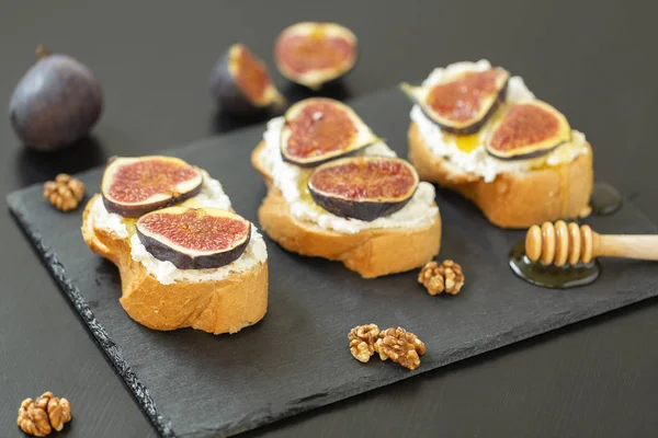 Ricotta sandviç, taze incir, ceviz ve siyah bir zemin üzerine kayrak bir tabakta bal