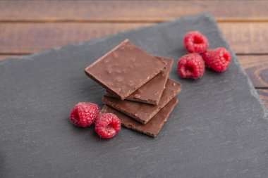 Yapılı-içinde kırmızı ahududu meyveleri ile çikolata bar yığını. Taze ahududu ve çikolata ahşap arka plan üzerinde.