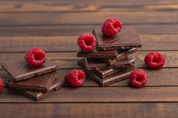 A stack of chocolate bars with built-in red raspberry berries. Fresh raspberries and chocolate on wooden background.