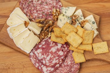 Farklı aperatifler ve mezeler karışımı. Dilim salam, kraker, Fransız camambert peyniri ile mavi küf bal ile ve ahşap zemin üzerine ceviz fındık.