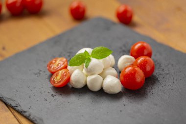 Mozzarella peyniri domates, roka ve baharatlar ile kayrak bir tabakta servis edilir