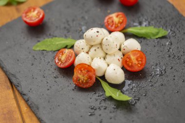 Mozzarella peyniri domates, roka ve baharatlar ile kayrak bir tabakta servis edilir