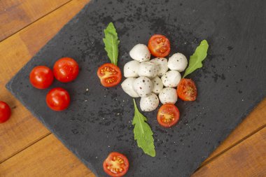 Mozzarella peyniri domates, roka ve baharatlar ile kayrak bir tabakta servis edilir