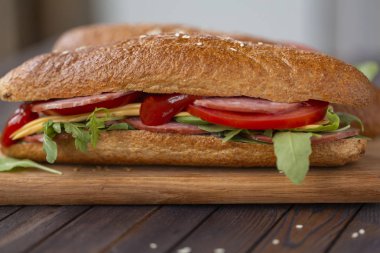 İki tane baget sandviç salam, peynir, roka salatası, domates ve soğan bir kesme tahtası üzerinde. Koyu ahşap arka plan üzerinde sandviç. Lezzetli Aperatif.