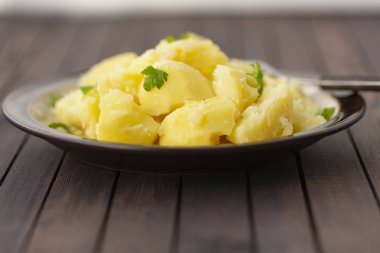 Taze ot ve ahşap bir masa üzerinde bir kasede yağ ile haşlanmış patates