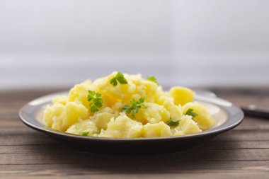 Taze ot ve ahşap bir masa üzerinde bir kasede yağ ile haşlanmış patates