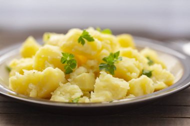 Taze ot ve ahşap bir masa üzerinde bir kasede yağ ile haşlanmış patates