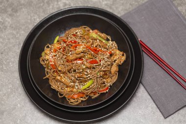 Kızarmış sebze, tavuk ve susam siyah bir kase erişte. Gri arka plan. Yakın çekim