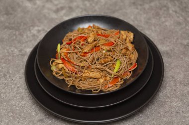 Kızarmış sebze, tavuk ve susam siyah bir kase erişte. Gri arka plan. Yakın çekim