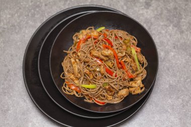 Kızarmış sebze, tavuk ve susam siyah bir kase erişte. Gri arka plan. Yakın çekim