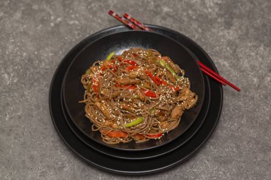 Kızarmış sebze, tavuk ve susam siyah bir kase erişte. Gri arka plan. Yakın çekim