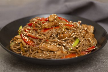 Kızarmış sebze, tavuk ve susam siyah bir kase erişte. Gri arka plan. Yakın çekim