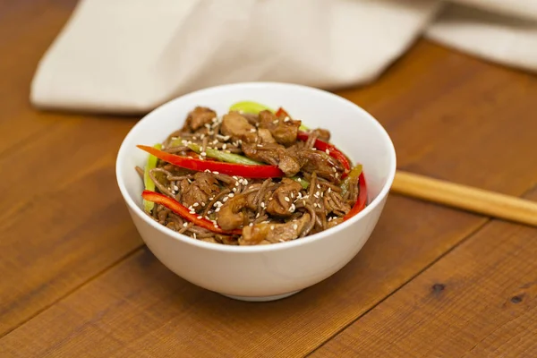 Asian noodles with chicken, vegetables and sesame. Rustic wooden background. Chopsticks. Close up. Dinner in the Asian style