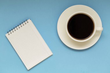 Üstten görünüm çalışma alanı mockup boş not defteri ve kahve fincanı ile mavi arka plan üzerinde. Metin girişi için Not defteri alanı. Düz yatıyordu.