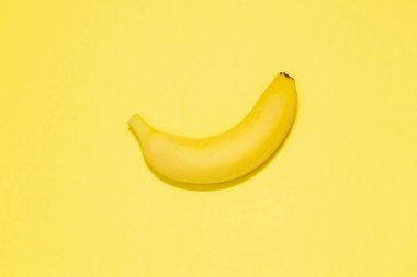 Tek muz sarı bir arka plan üzerinde. Üstten görünüm. Metin için yer. Minimalist kavramı. 