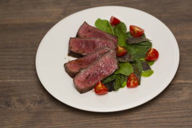 Yeşil salata ve domates beyaz tabakta ile sulu biftek Orta nadir sığır eti