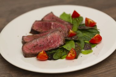 Yeşil salata ve domates beyaz tabakta ile sulu biftek Orta nadir sığır eti