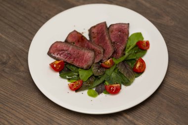 Yeşil salata ve domates beyaz tabakta ile sulu biftek Orta nadir sığır eti