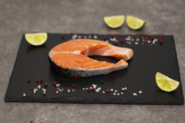 Kireç ve baharatlar ile yemek pişirmek için hazırlanan somon steak çiğ balık. Siyah arduvaz gemide üstten görünüm. 