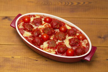 Ahşap bir masa üzerinde bir pişirme çanağı domates soslu köfte. Seçici odak