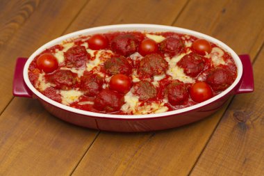 Ahşap bir masa üzerinde bir pişirme çanağı domates soslu köfte. Seçici odak