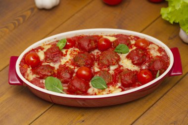 Ahşap bir masa üzerinde bir pişirme çanağı domates soslu köfte. Seçici odak