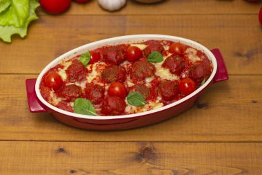 Ahşap bir masa üzerinde bir pişirme çanağı domates soslu köfte. Seçici odak