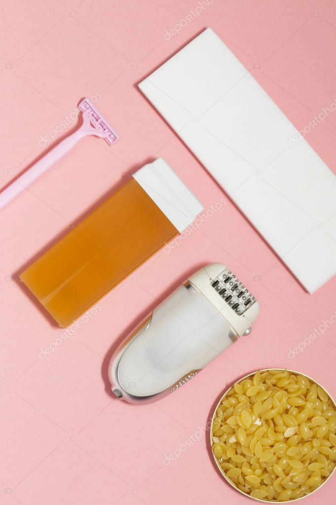 Beauty, depilation and hair removal concept - wax, spatula, epilator and safety razor on pink background. Top view.
