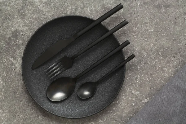 Black plate, cutlery on stone table top view. Table setting.