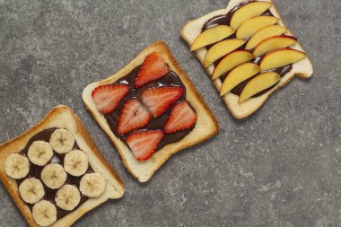 Lezzetli kızarmış ekmek ekmek taze çilek, muz, şeftali ve çikolatalı hamur gri arka plan üzerinde. Lezzetli kahvaltı. Üstten Görünüm