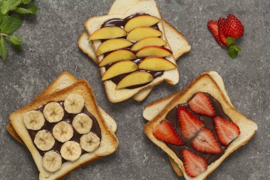Lezzetli kızarmış ekmek ekmek taze çilek, muz, şeftali ve çikolatalı hamur gri arka plan üzerinde. Lezzetli kahvaltı. Üstten Görünüm