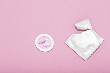 Prezervatif ve prezervatif paketi pembe bir arka plan üzerinde açıldı. Gebelik ya da cinsel yolla bulaşan hastalık (Std) olasılığını azaltmak için prezervatif kullanın. Güvenli seks ve üreme sağlık kavramı.