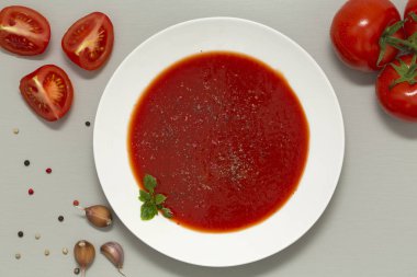 Gri arka plan üzerinde beyaz bir kase domates çorbası. Lezzetli çorba domates ve sarımsak ve baharat ile taze otlar. Üstten Görünüm.