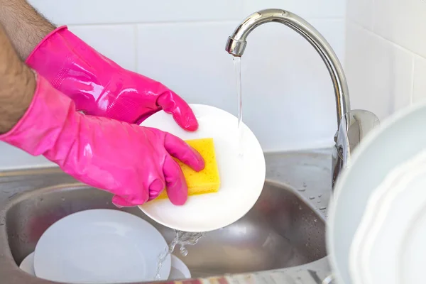 Close up washing dishes. Male hands in foam washes the crockery with a detergent and sponge in the kitchen of the house.