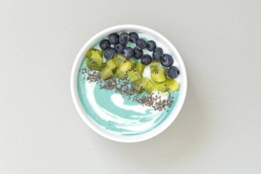 Mavi spirulina smoothie kase üst görünümü yaban mersini, kivi, Chia tohumu ve gri masada granola ile. Sağlıklı kahvaltı. Vegan gıda. 