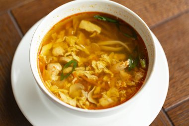 Ahşap bir masada bir kase tavuk, sebze ve yumurta ile Asya şehriye çorbası.