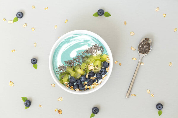Top view of blue spirulina smoothie bowl with blueberries, kiwi, Chia seeds and granola on grey table. Healthy breakfast. Vegan food. 