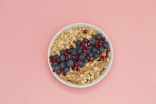 Smoothie bowl with blueberries, pomegranates and granola. Breakfast smoothie bowl on pink background, top view. Vegan diet food concept.