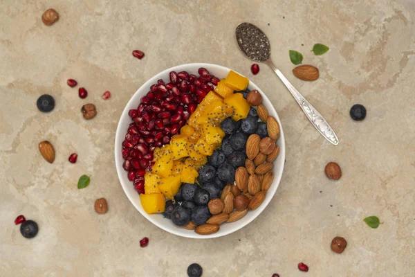 Top view of a smoothie bowl with fresh ripe blueberry, nuts, chia, mango and pomegranate. The concept of healthy eating and lifestyle.