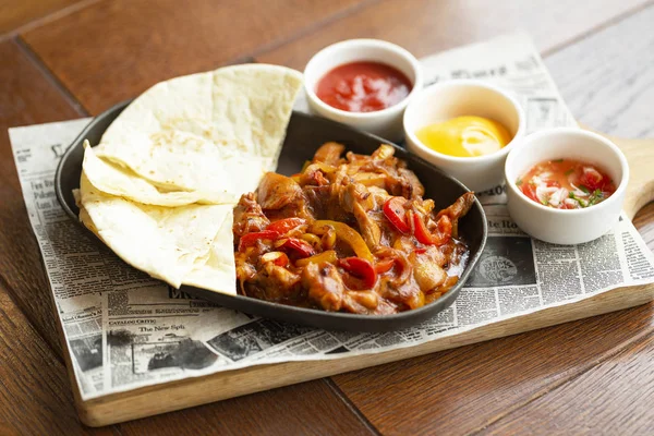 Soğan ve renkli biber ile Sığır Fajitas, tortilla, peynir sosu, salsa ve domates sosu ile servis edilir. Meksika'nın geleneksel yemeği. Seçici odak. Ahşap arka plan.