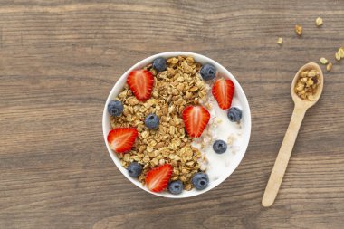 Ahşap arka plan üzerinde granola, yoğurt, çilek ve taze yaban mersini ile Sağlıklı smoothie kase. Kahvaltı smoothie kase, üst görünümü.