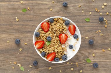 Ahşap arka plan üzerinde granola, yoğurt, çilek ve taze yaban mersini ile Sağlıklı smoothie kase. Kahvaltı smoothie kase, üst görünümü.