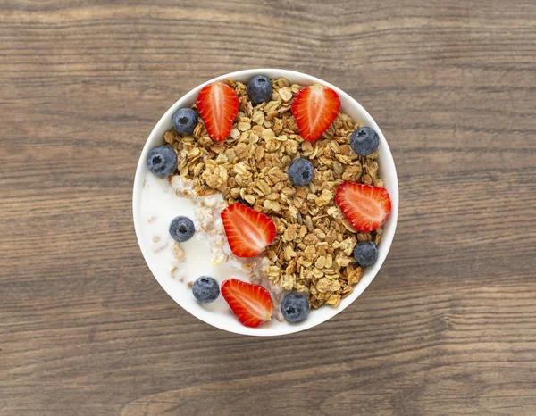 Healthy smoothie bowl with granola, yogurt, strawberry and fresh blueberries on wooden background. Breakfast smoothie bowl, top view.