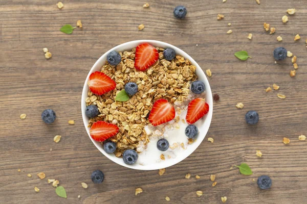 Healthy smoothie bowl with granola, yogurt, strawberry and fresh blueberries on wooden background. Breakfast smoothie bowl, top view.