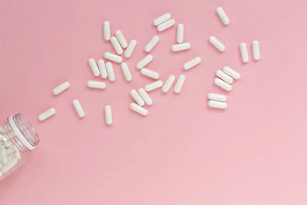 Capsules pills white on pink background. Heap of pills. Medical supplies. Natural supplements and vitamins.