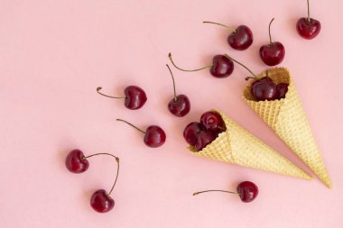 Waffle konilerinde taze kiraz. Dondurma konisi pembe bir arka plan üzerinde taze kiraz ile dolu. Üst te. Kopya alanı. Yaz konsepti.  